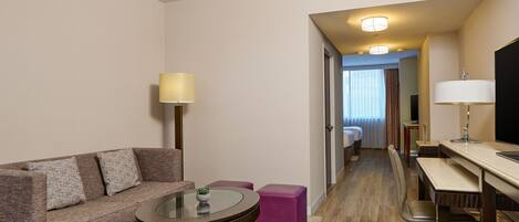 Een hotelkamer met een bank, een klein rond tafeltje, een bureau met stoel en een bed op de achtergrond.