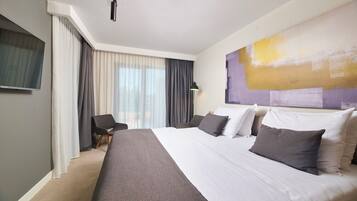 A hotel room with a large bed, a flat-screen TV, a chair, and a window with curtains.