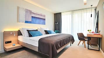 Una habitación de hotel moderna con cama, mesita de noche, escritorio, silla y un cuadro abstracto grande en la pared.