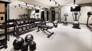 A modern gym with various equipment including dumbbells, a bench press, and cardio machines.