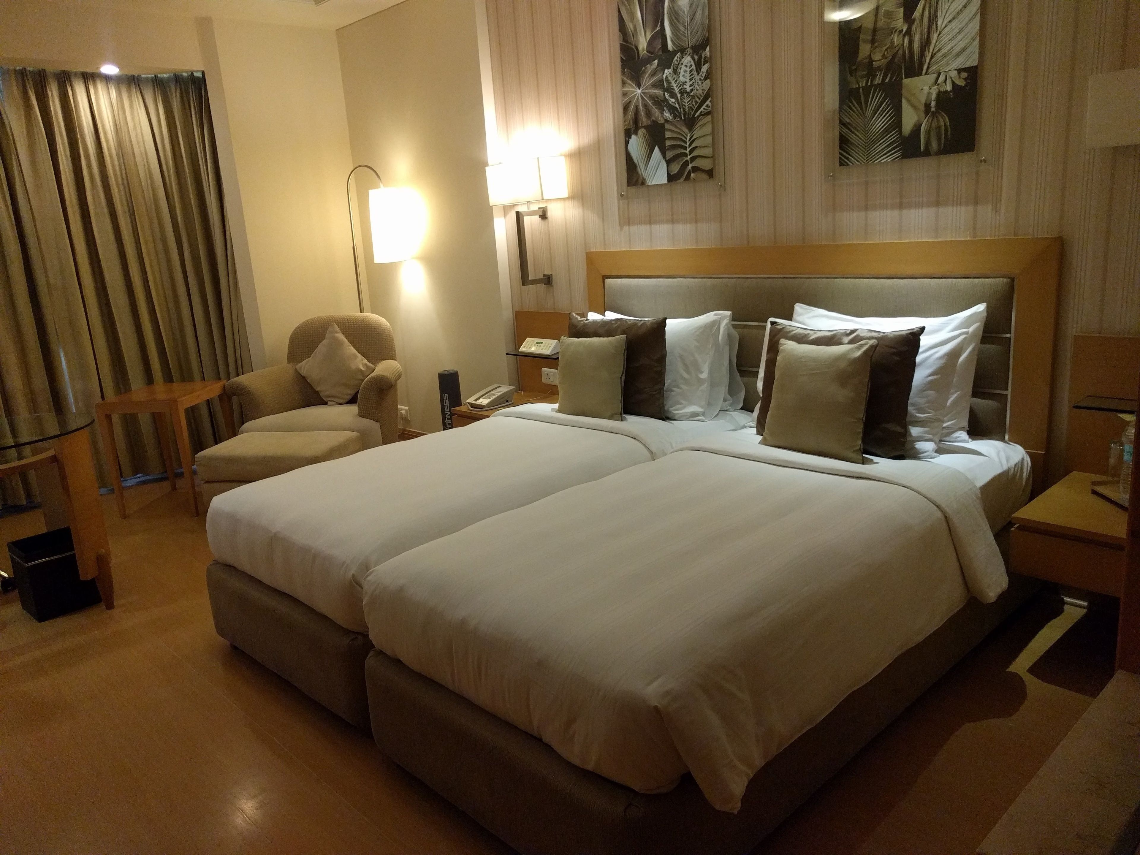 A hotel room with two large beds, a sitting area with a chair, a desk, and a lamp.