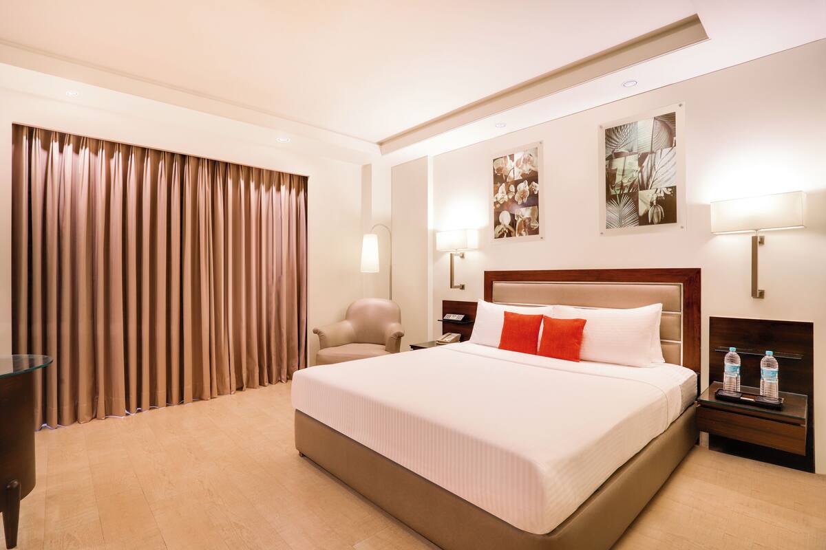 Ein Hotelzimmer mit einem großen Bett, einem Sessel, einem Nachttisch mit Lampe und einem Wandbild.