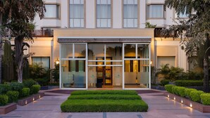 Un hôtel moderne doté d’une façade en verre, d’un jardin bien entretenu et d’une entrée accueillante.