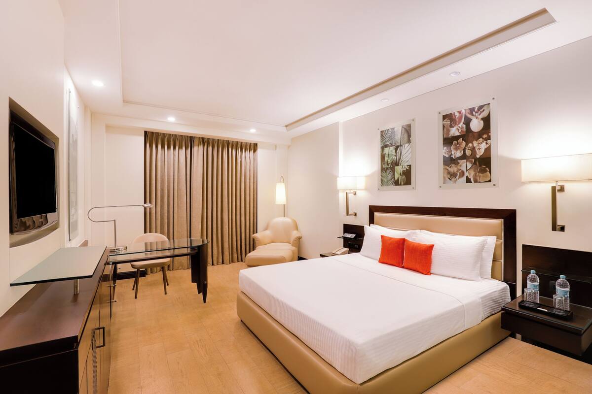 Ein Hotelzimmer mit Bett, Schreibtisch, Sessel, Fernseher und Kunstwerken an den Wänden.