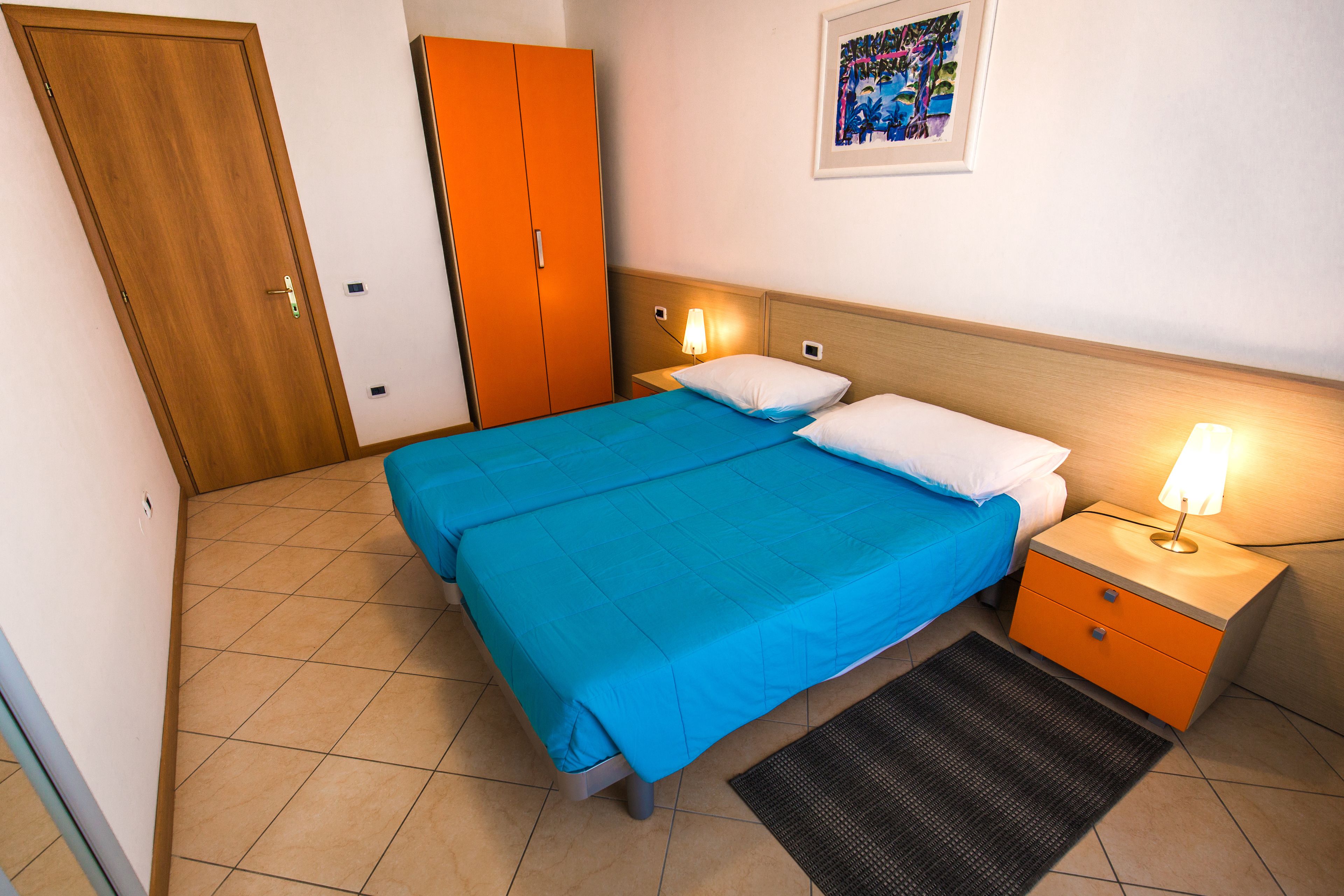A hotel room with a bed, nightstands, a wooden wardrobe, and a framed picture on the wall.