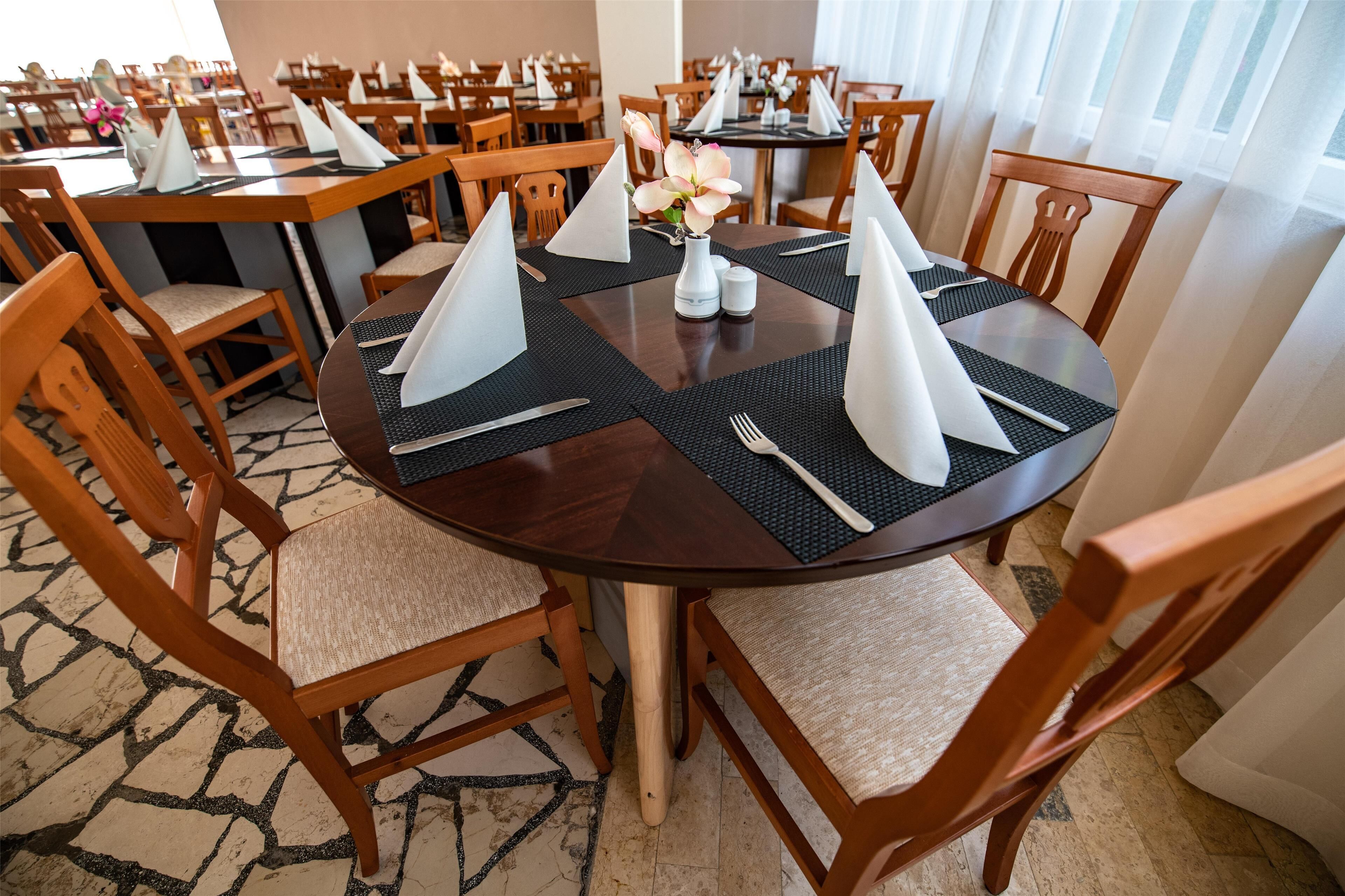 A dining area with round tables set with placemats, napkins, and cutlery.