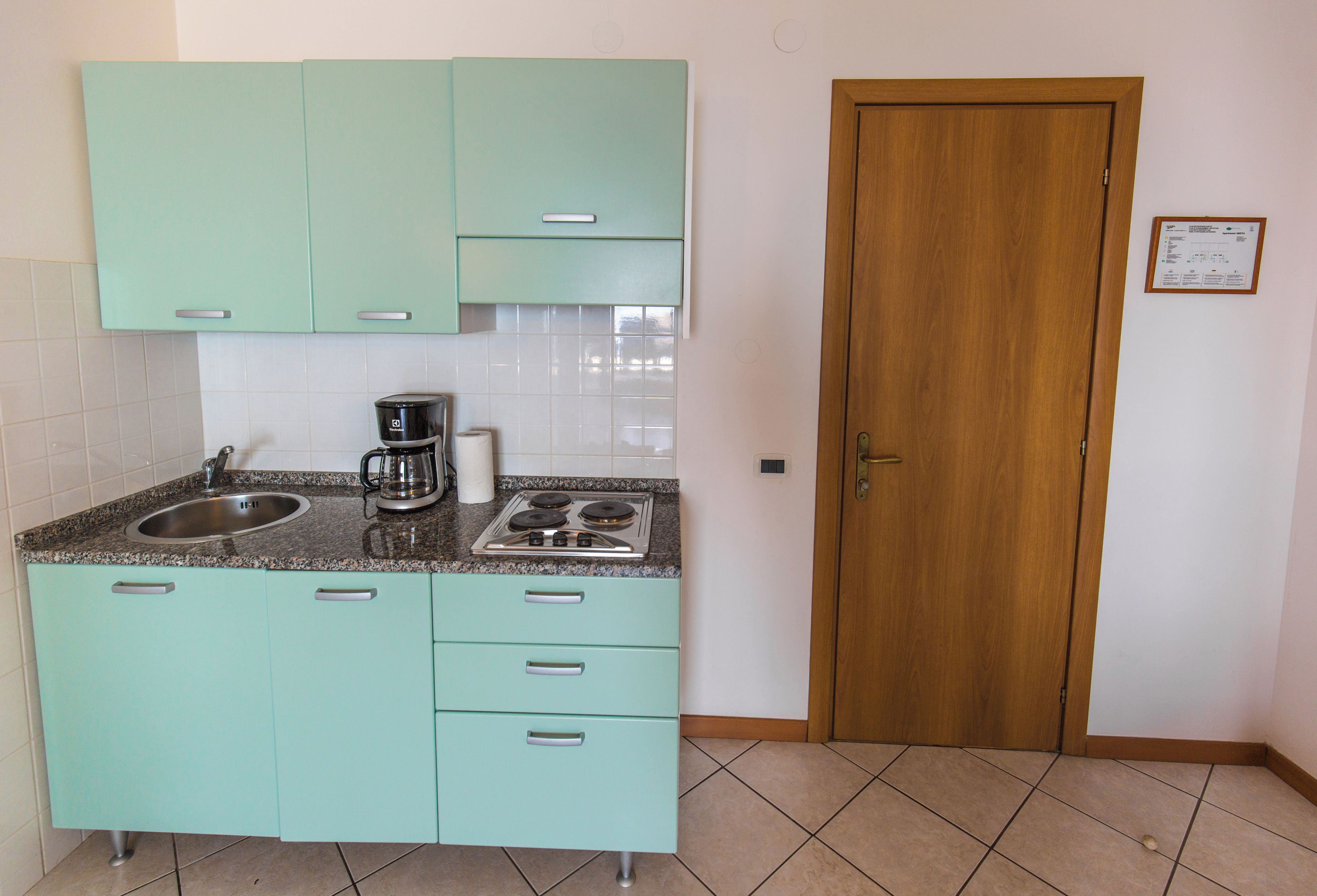 A kitchen with teal cabinets, a double sink, a coffee maker, and a stove.
