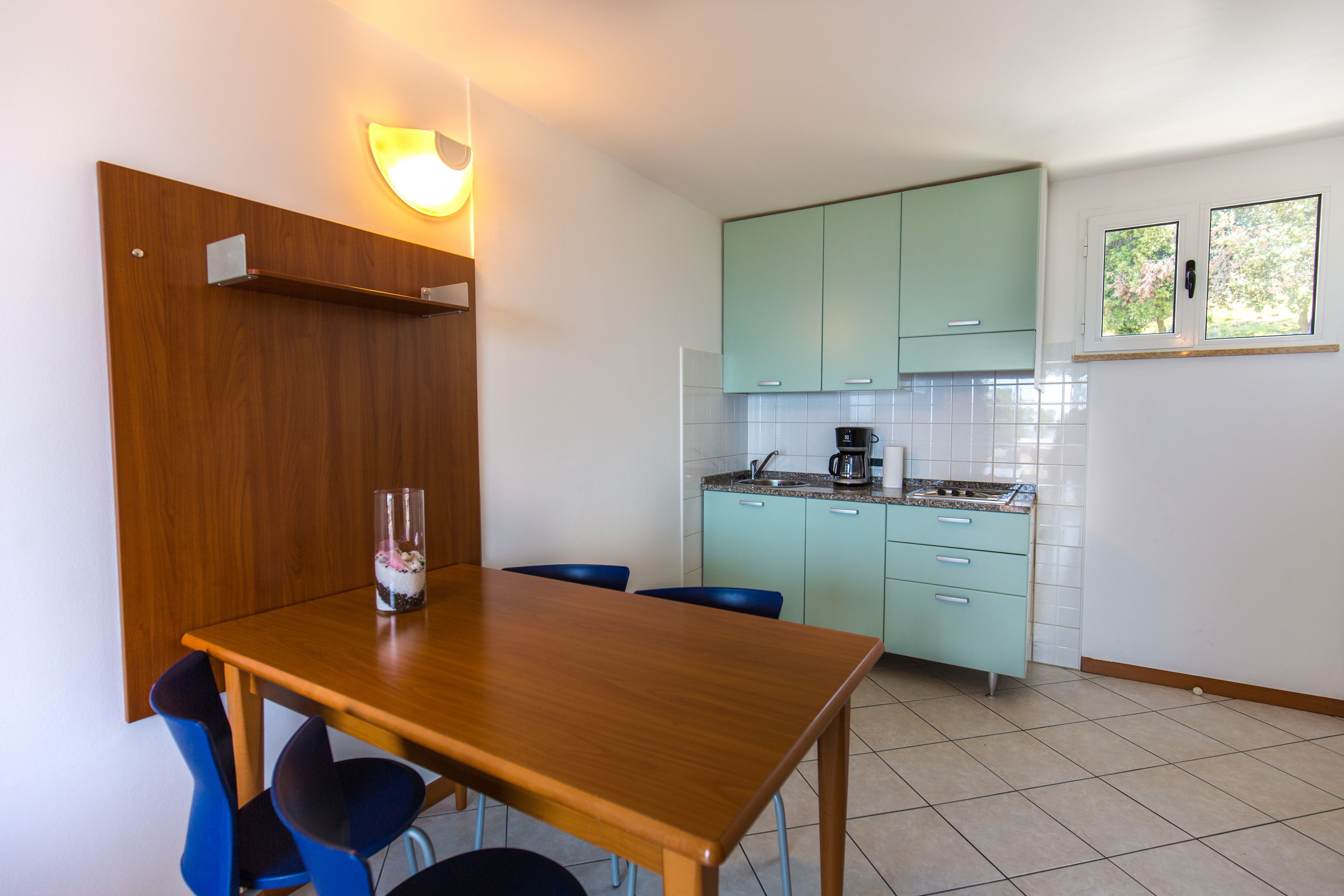 Une cuisine de taille réduite avec des meubles de couleur turquoise, une table à manger en bois et des chaises.