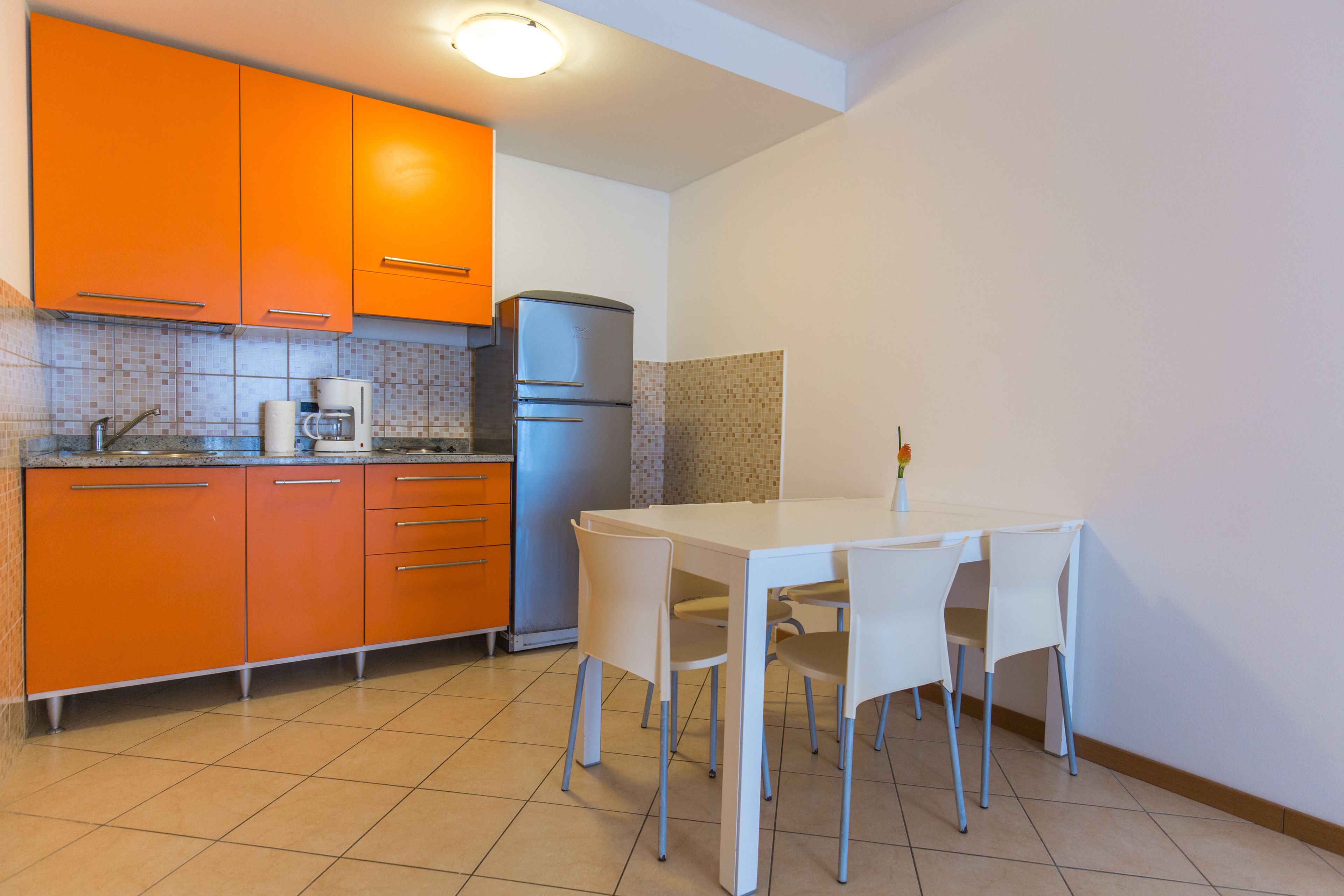 A kitchen with orange cabinets, a white table, and four chairs.
