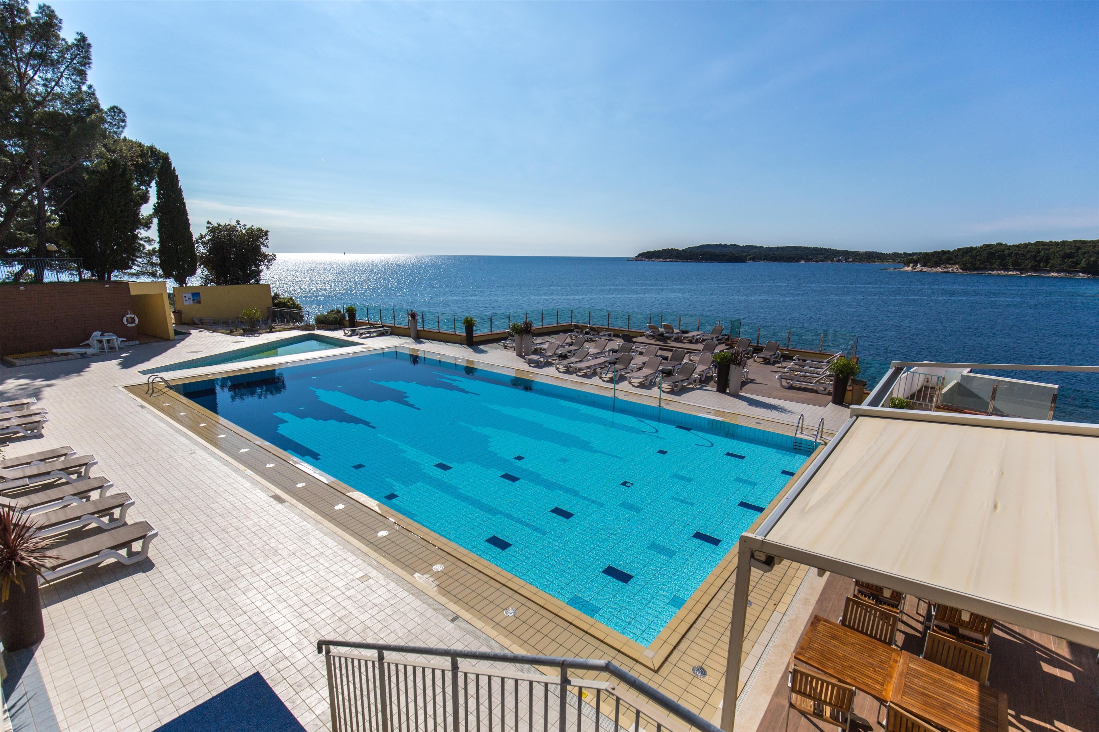 A swimming pool with clear blue water, surrounded by lounge chairs and a deck area with a view of the sea.