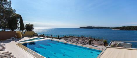 Une piscine à l’eau cristalline, entourée de chaises longues et d’une terrasse offrant une vue sur la mer.