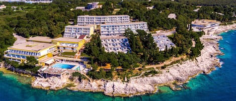 An aerial view of a coastal hotel with multiple buildings, a swimming pool, and a rocky shoreline.