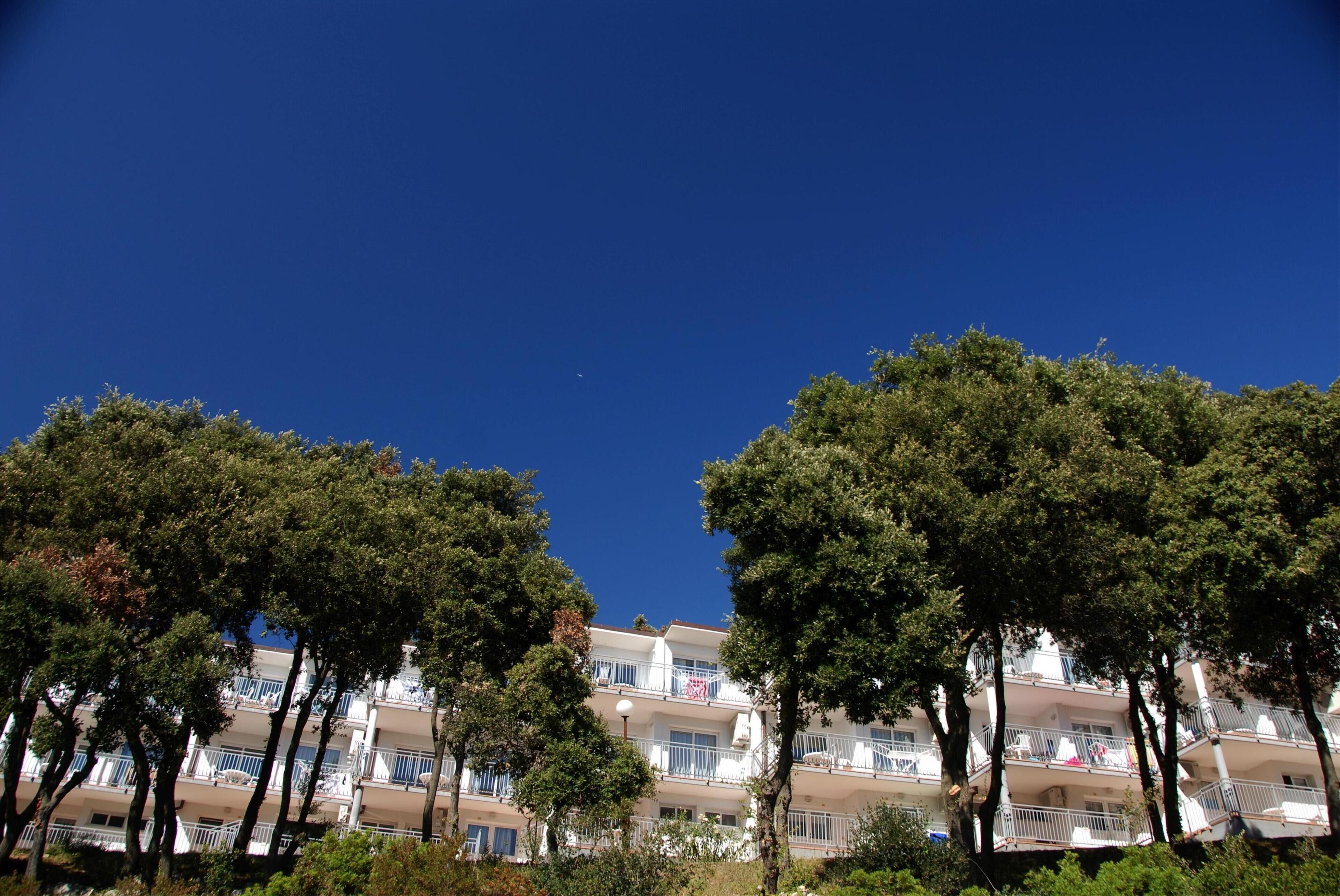Un hotel a più piani con balconi, circondato da alberi.