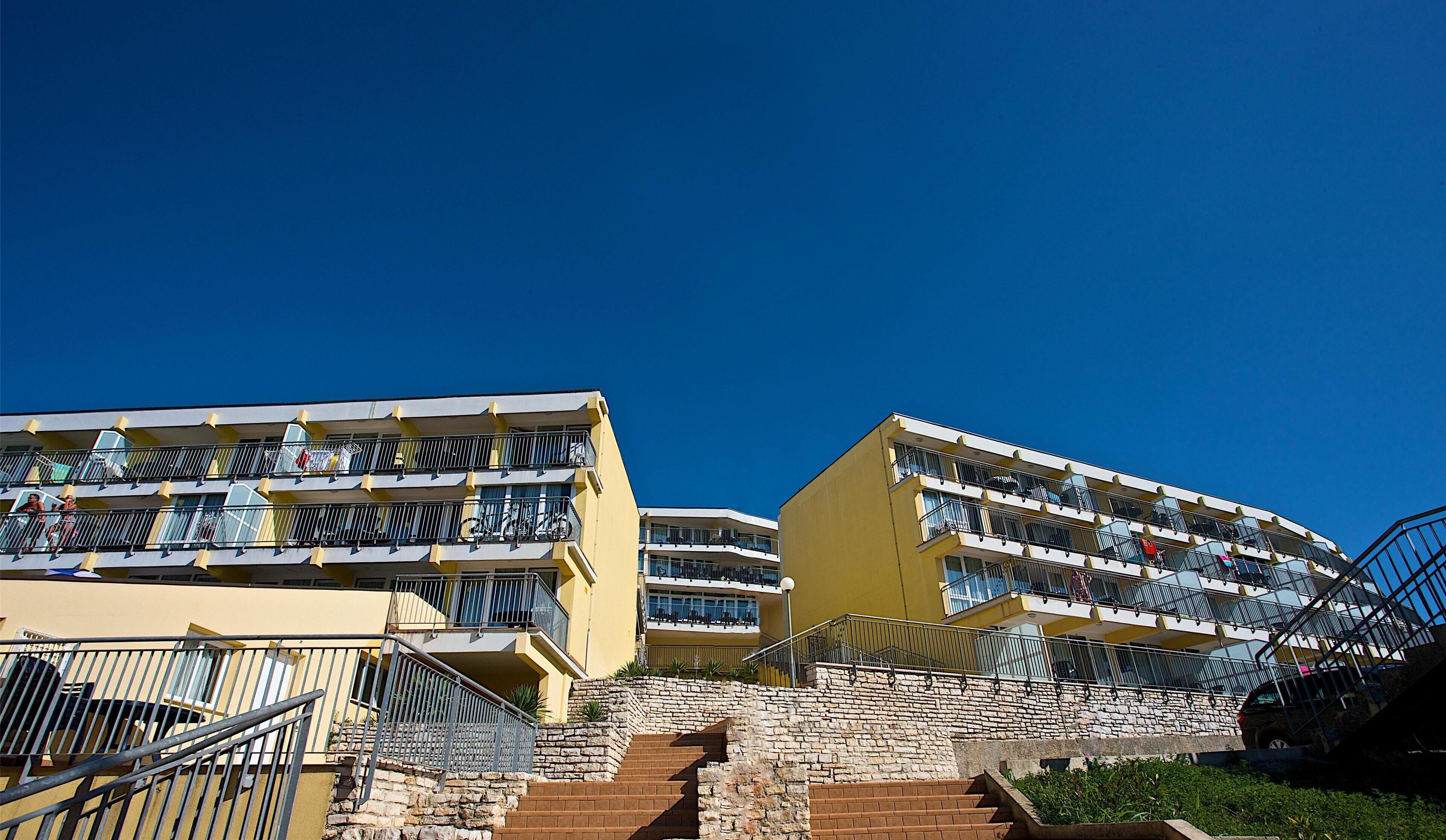 A multi-story hotel with balconies, a stone staircase, and a clear blue sky.