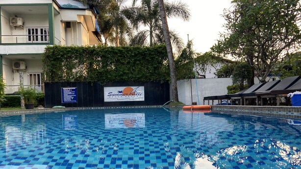 A swimming pool with a checkered tile pattern, surrounded by greenery and a sign for Summer Ville Beach Resort. - Summerville Beach Resort (Candolim)