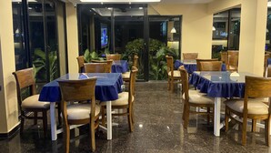 A restaurant with tables and chairs, a ceiling fan, and a TV screen. - Summerville Beach Resort (Candolim)