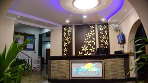 A reception area with a modern design, featuring a reception desk, a large digital display, and decorative wall panels. - Summerville Beach Resort (Candolim)