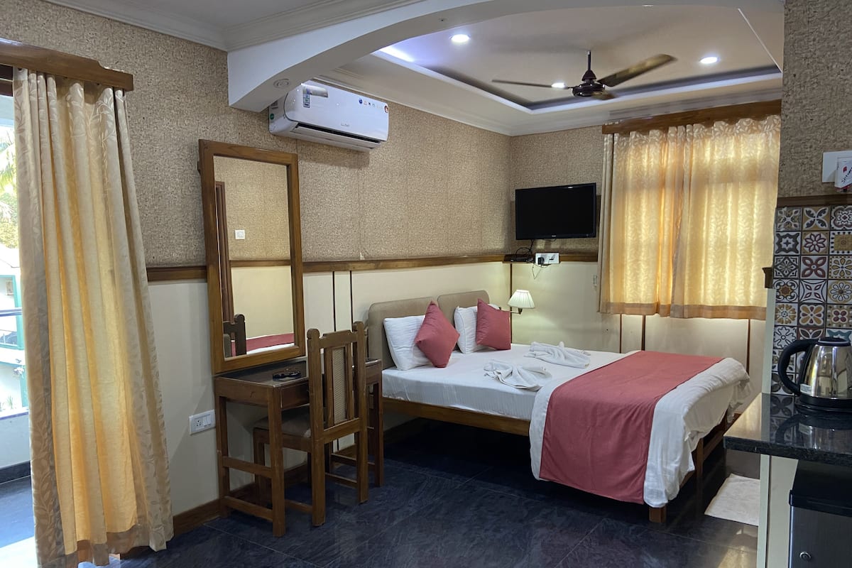 A hotel room with a bed, a desk, a chair, a TV, and an air conditioning unit.