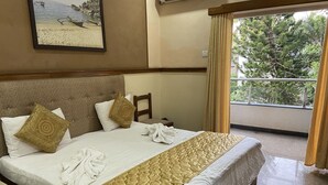 A hotel room with a large bed, a headboard with a decorative pattern, and a view of trees through the window. - Summerville Beach Resort (Candolim)
