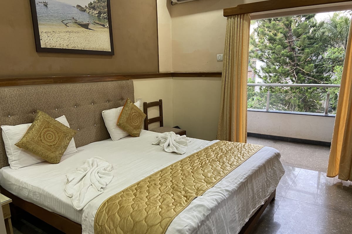 A hotel room with a large bed, a headboard with a decorative pattern, and a view of trees through the window.