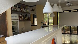 A bar area with white pendant lights, a refrigerated display, and a sign for 'Sunshine Pub & Restaurant'. - Summerville Beach Resort (Candolim)