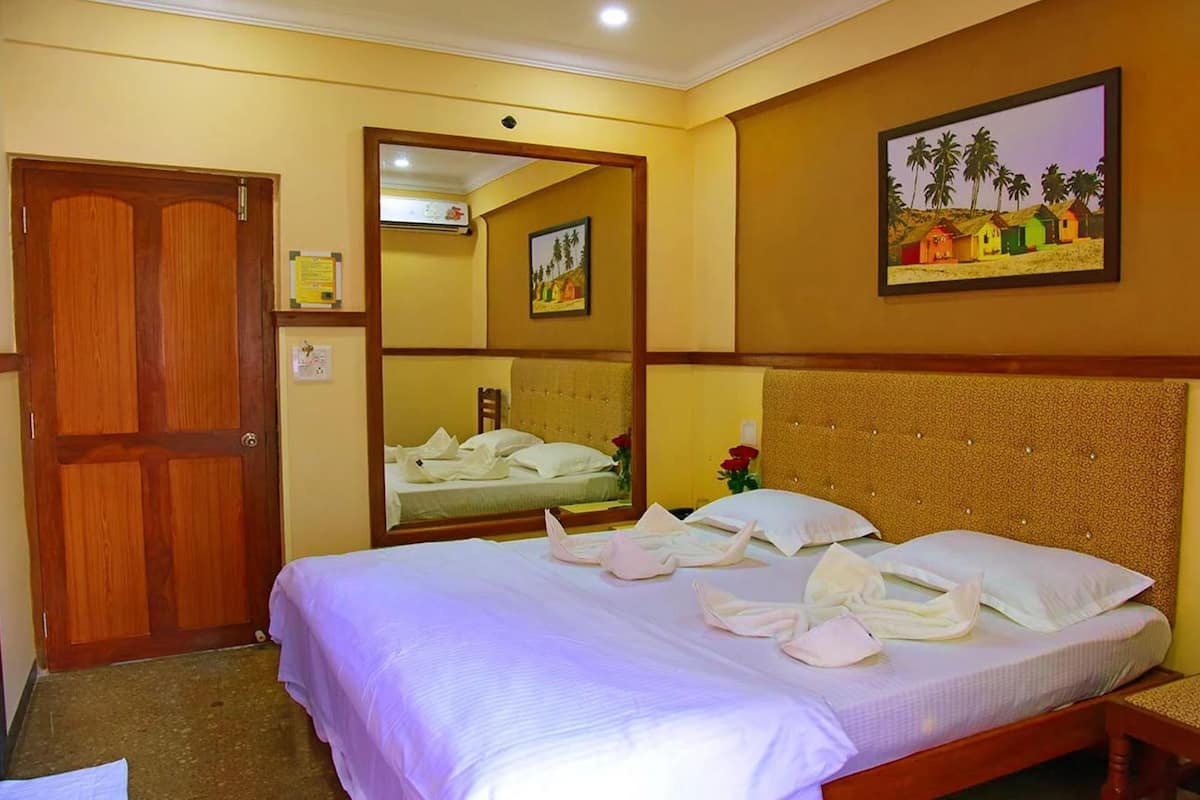 A hotel room with a bed, a wooden door, a mirror, and a painting on the wall.