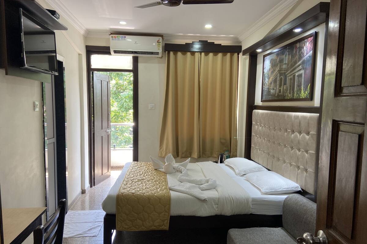 A hotel room with a bed, a bedside table, an air conditioning unit, a door, and a window with curtains.