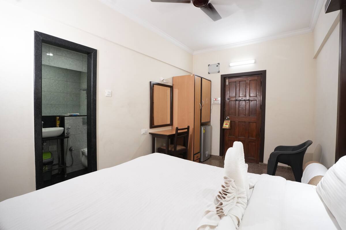 A hotel room with a bed, a desk, a chair, a wardrobe, and a shower area.