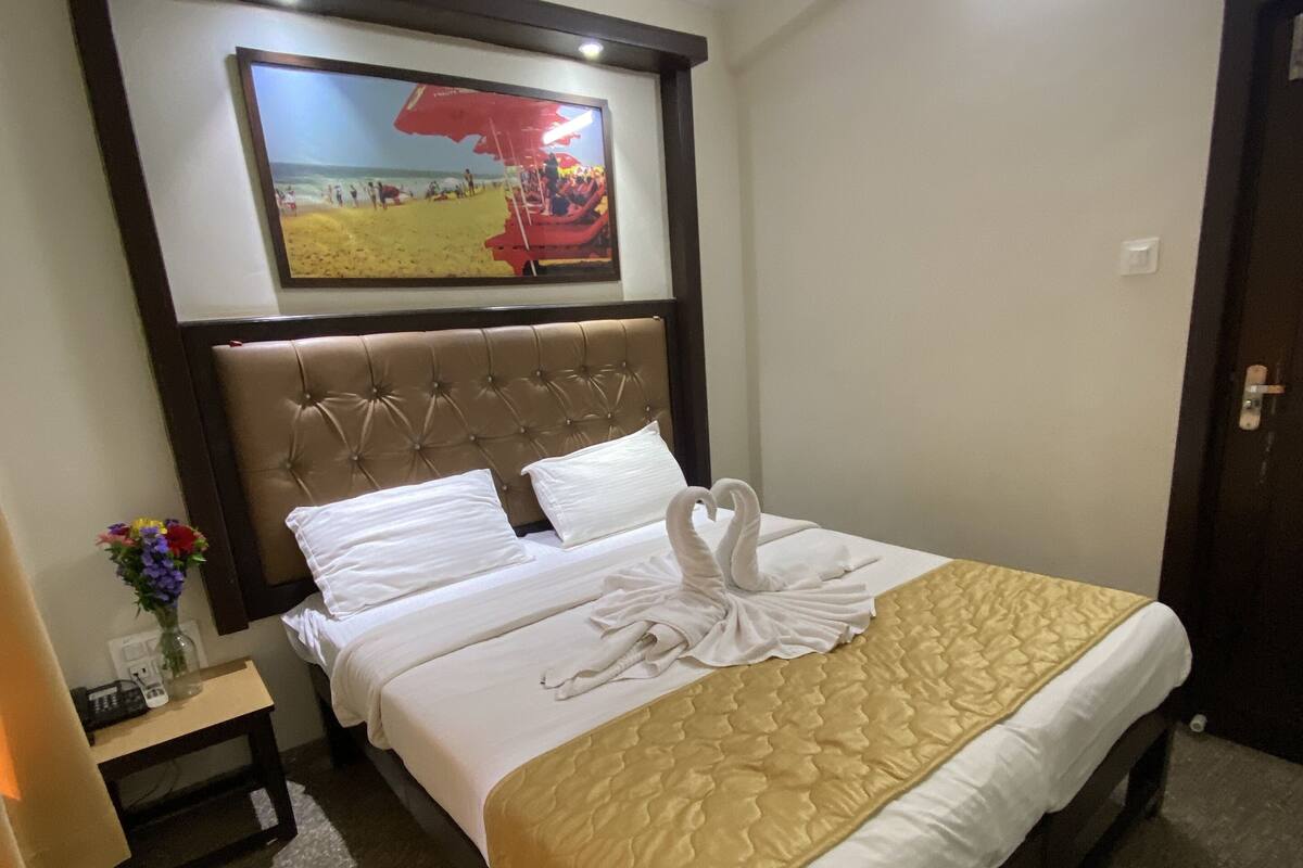 A hotel room with a bed, a headboard, a nightstand with a vase of flowers, and a painting on the wall.