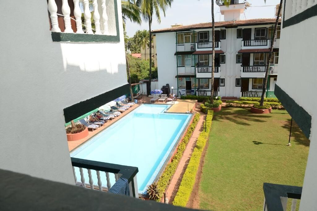 A hotel with a swimming pool, a well-maintained lawn, and a multi-story building with balconies.