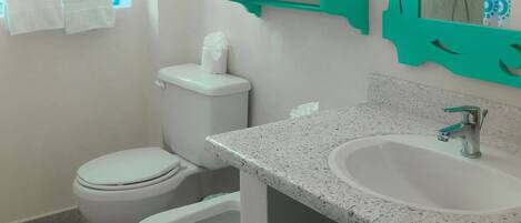 A bathroom with a toilet, bidet, sink, and a mirror with a teal frame.