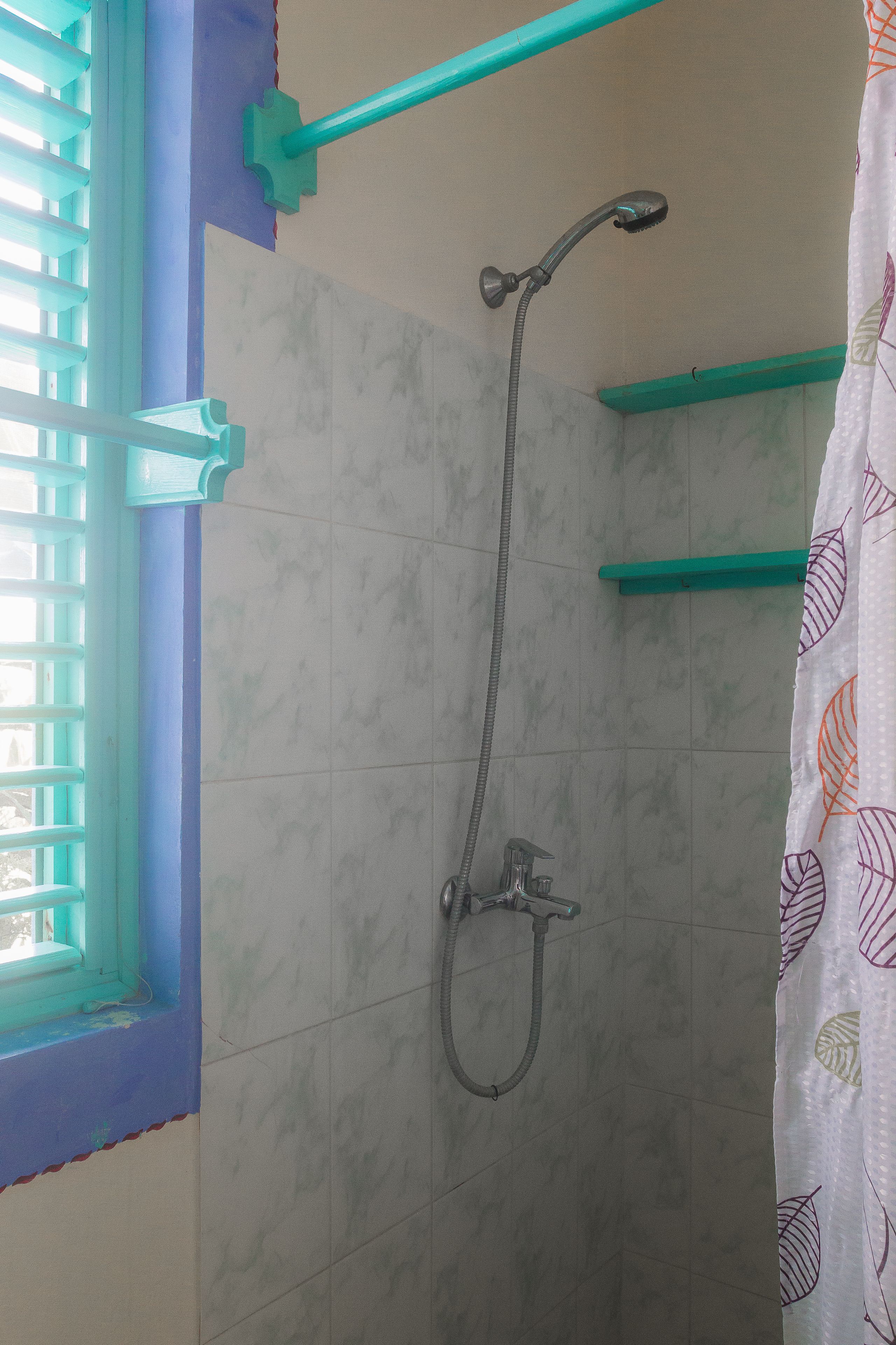 A shower area with a handheld showerhead, a wall-mounted faucet, and a window with blue trim.