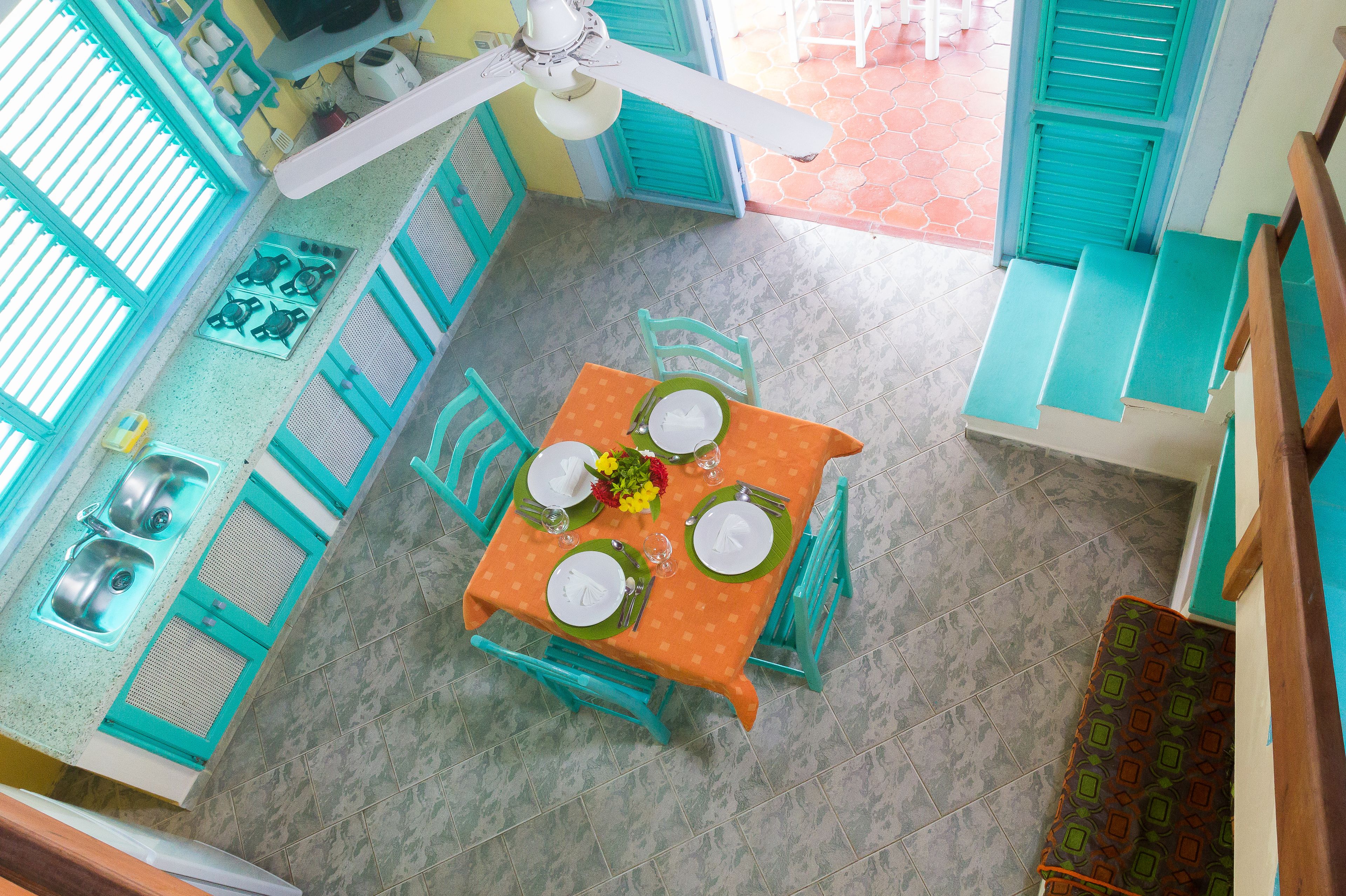 A kitchen with a gas stove, sink, and blue cabinets. There is a dining table set with plates, glasses, and a flower centerpiece.