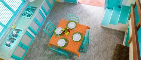 A kitchen with a gas stove, sink, and blue cabinets. There is a dining table set with plates, glasses, and a flower centerpiece.