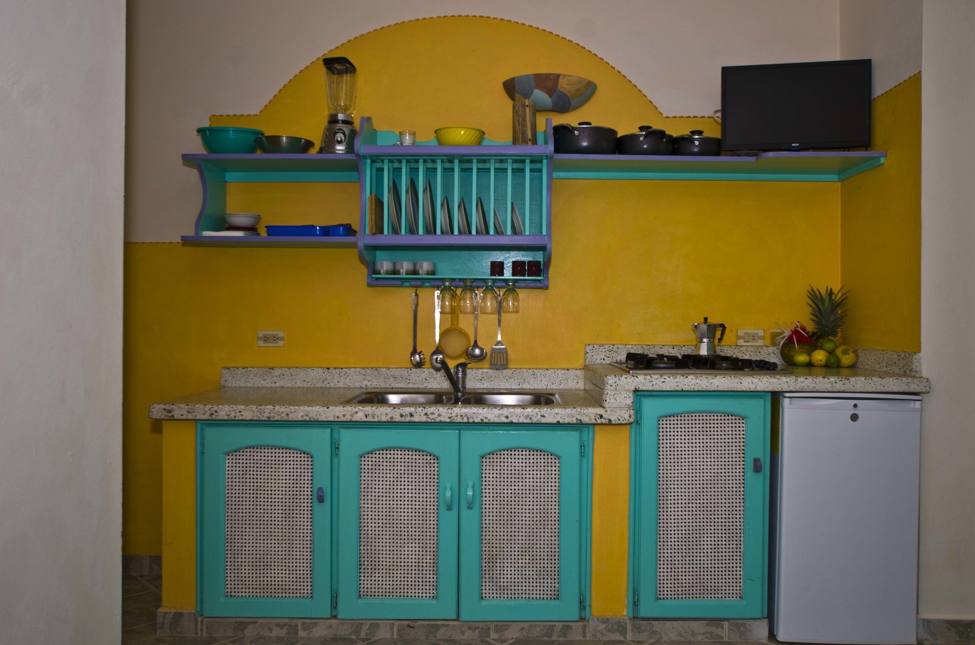 A kitchen with teal cabinets, a yellow wall, and a small refrigerator.