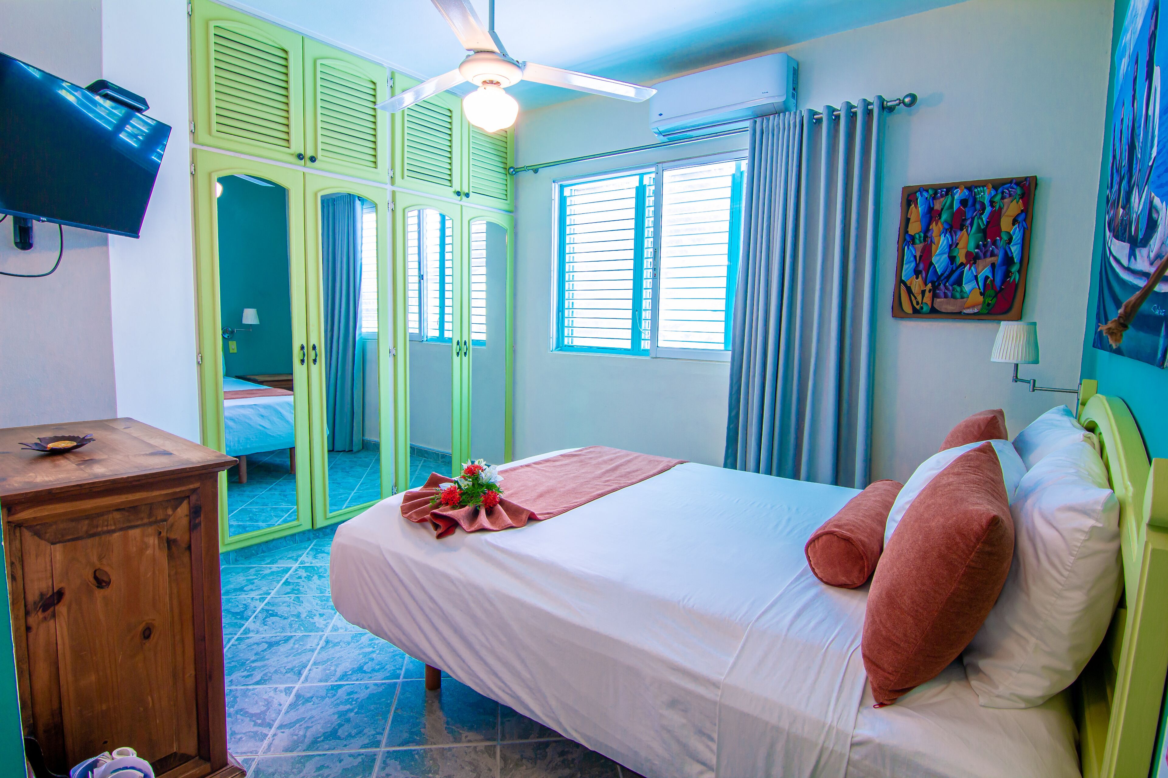Une chambre d’hôtel avec un lit, une armoire en bois, un ventilateur de plafond et un téléviseur.