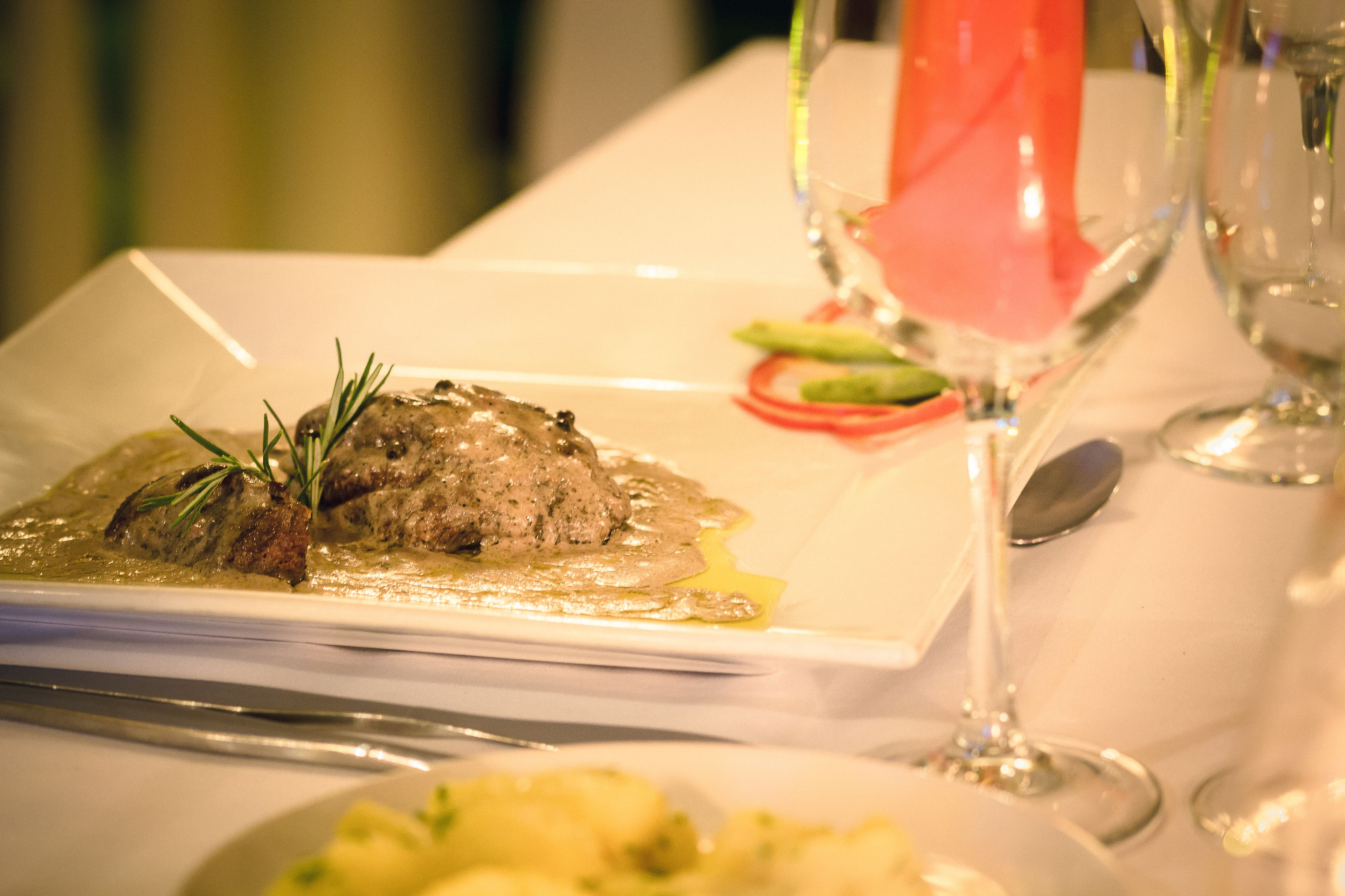 A plated dish with a garnish, a spoon, and a glass of red wine on a table.
