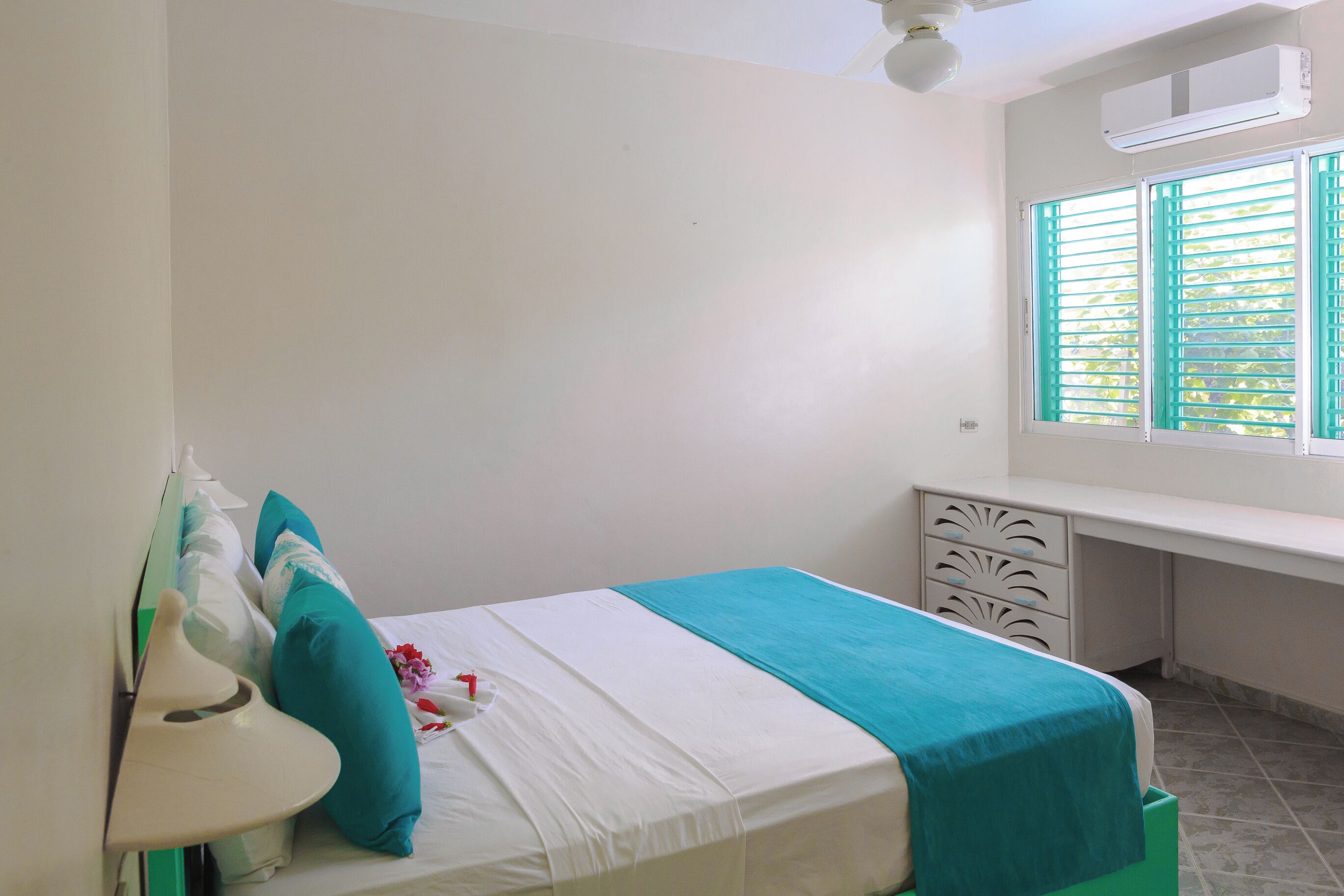 A bedroom with a bed, a desk, and a window with shutters.