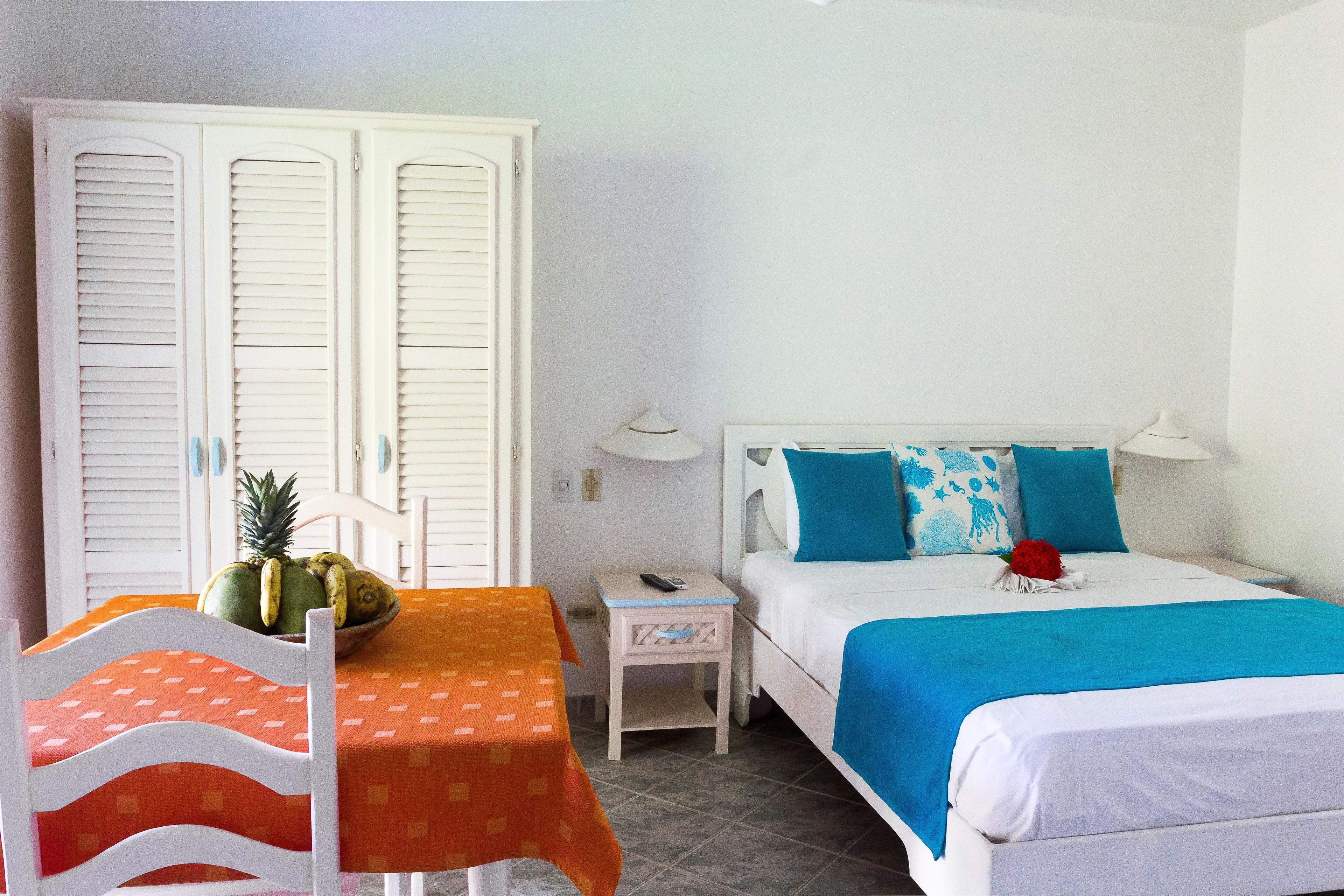 Un dormitorio con una cama, una mesita de noche, una mesa con fruteros y una silla.