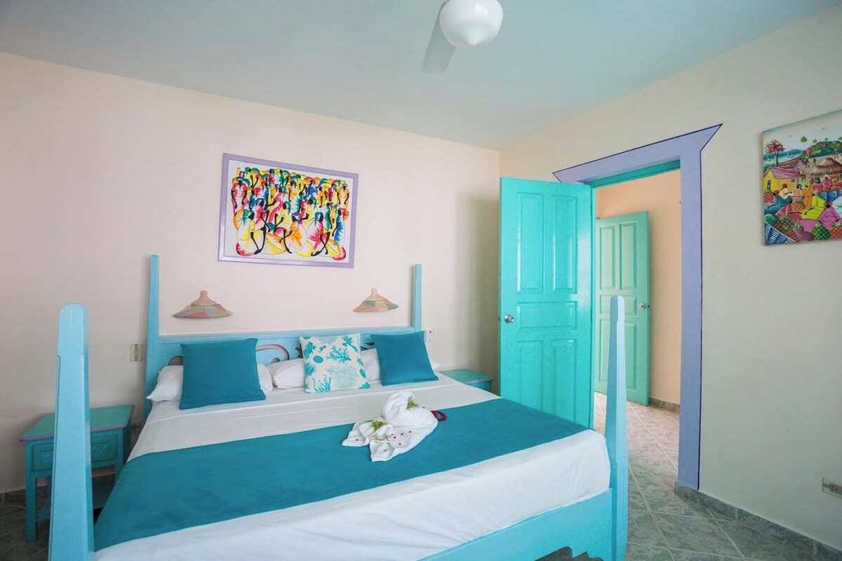 A bedroom with a bed, a painting, and a door.