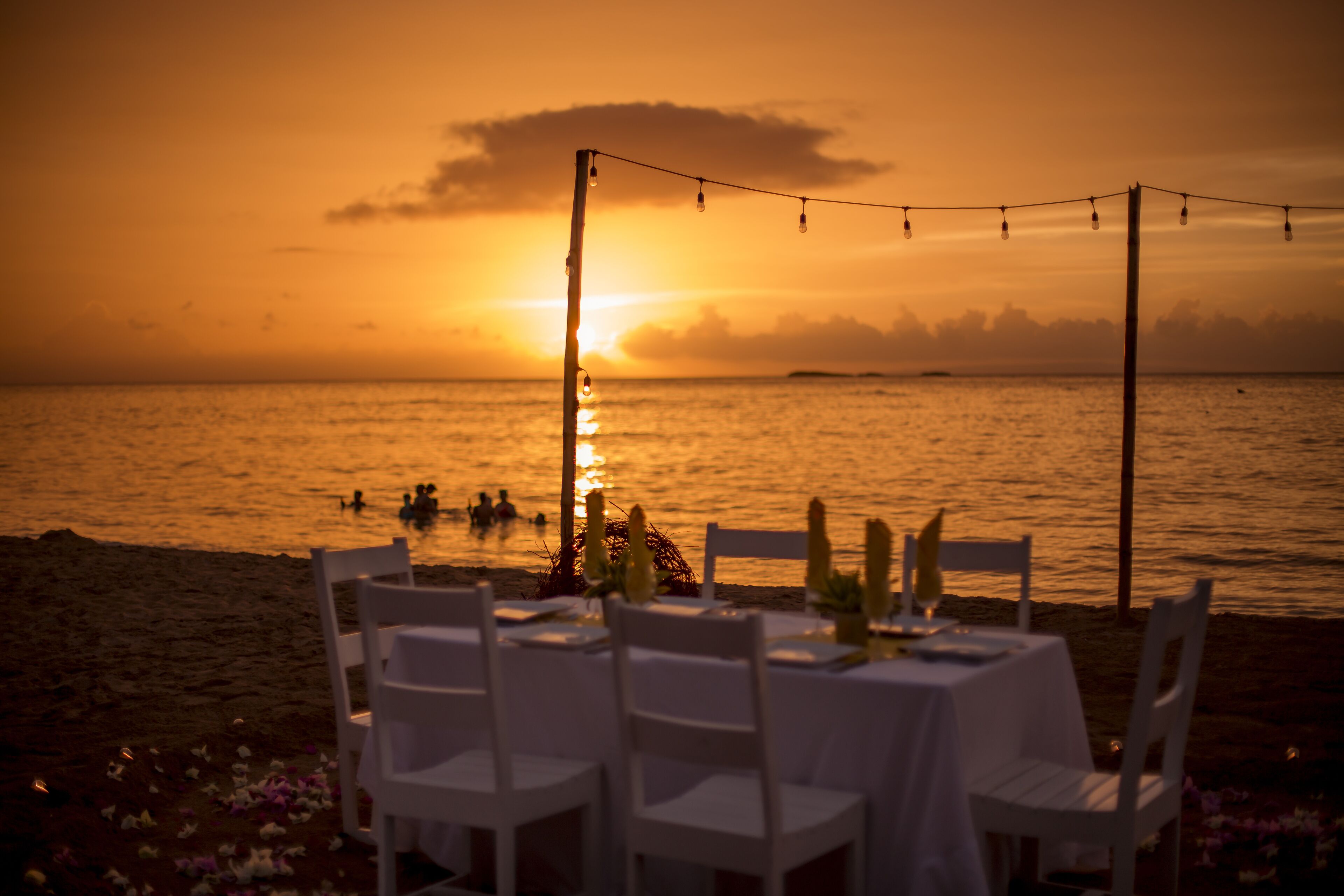 Una vista del atardecer sobre el océano, con una mesa lista para comer en la playa.