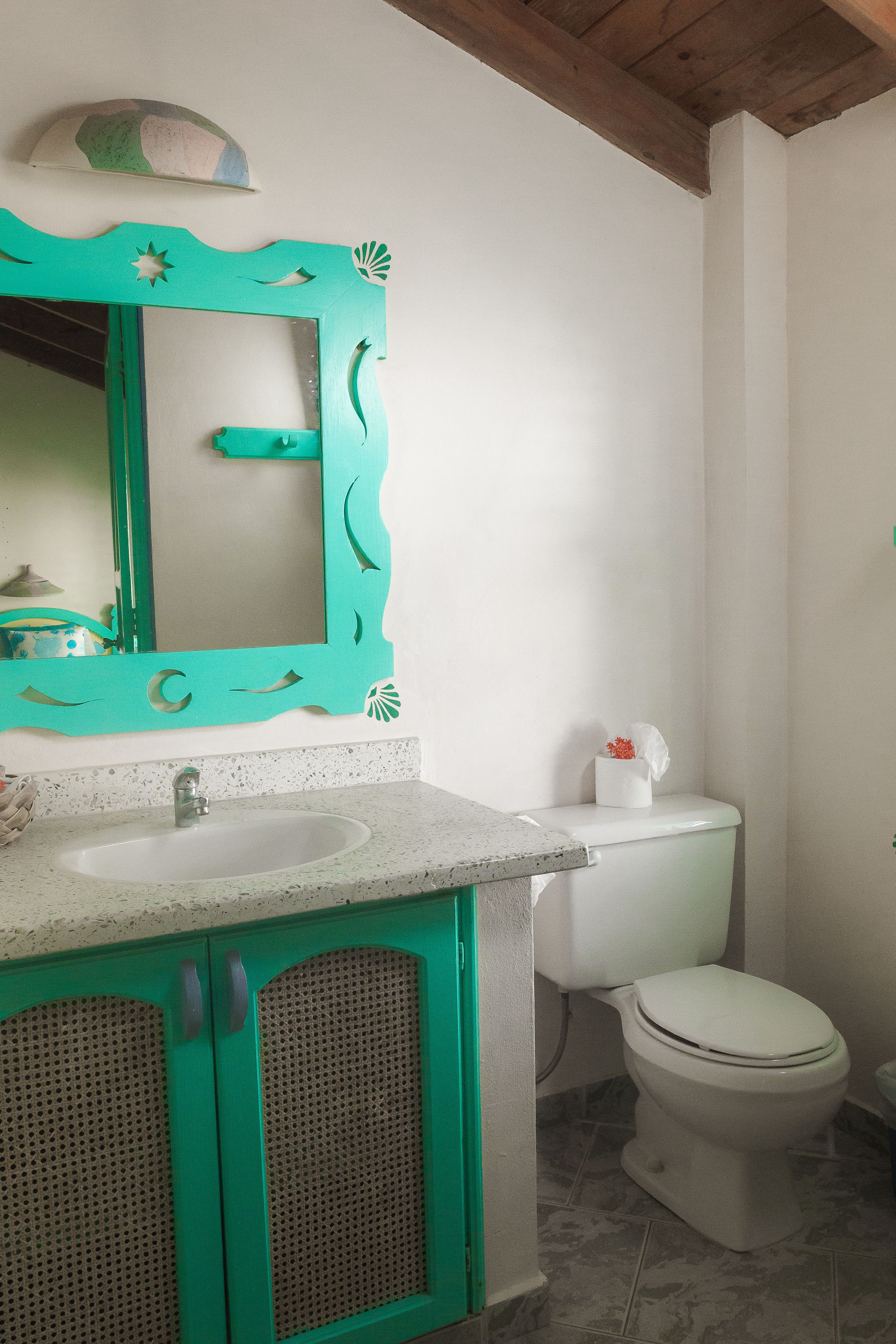 A bathroom with a white sink, a green vanity, a toilet, and a mirror with a decorative frame.