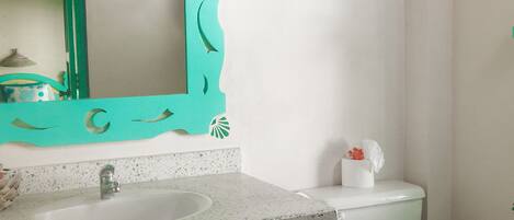 A bathroom with a white sink, a green vanity, a toilet, and a mirror with a decorative frame.