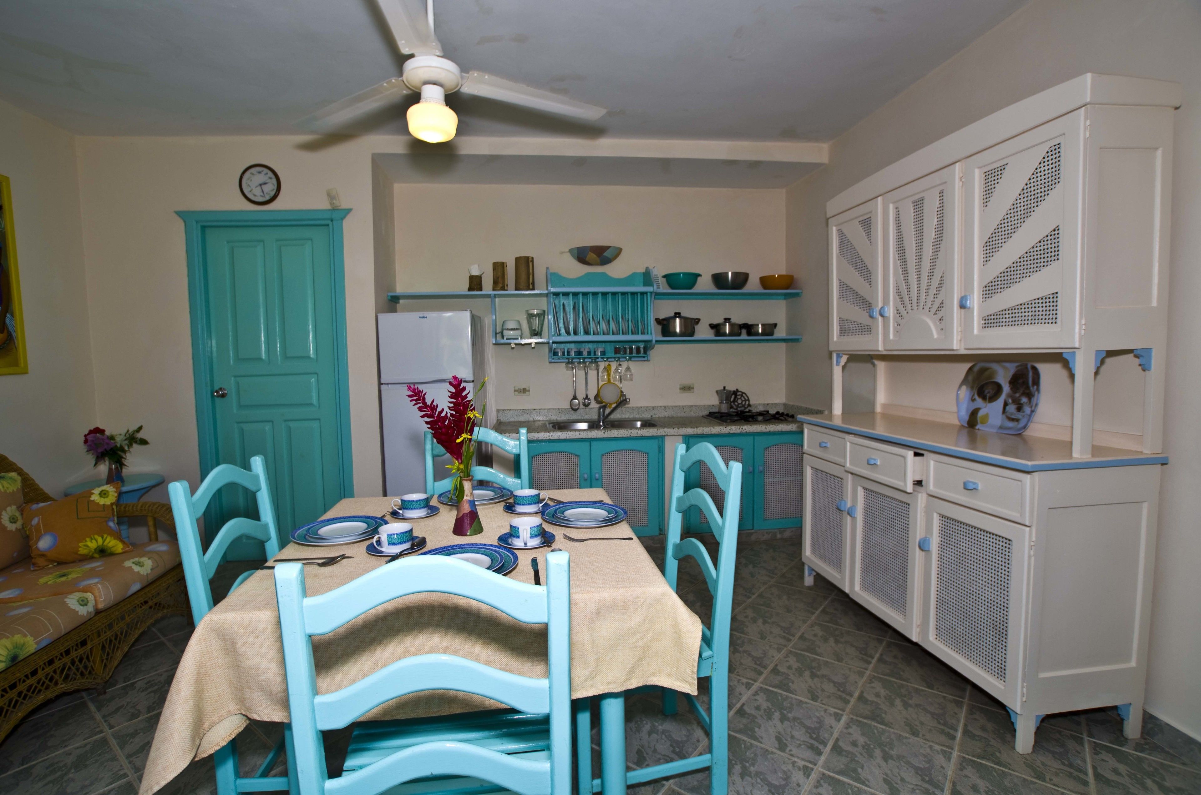 A kitchen with teal cabinetry, a dining table set with plates, and a ceiling fan.
