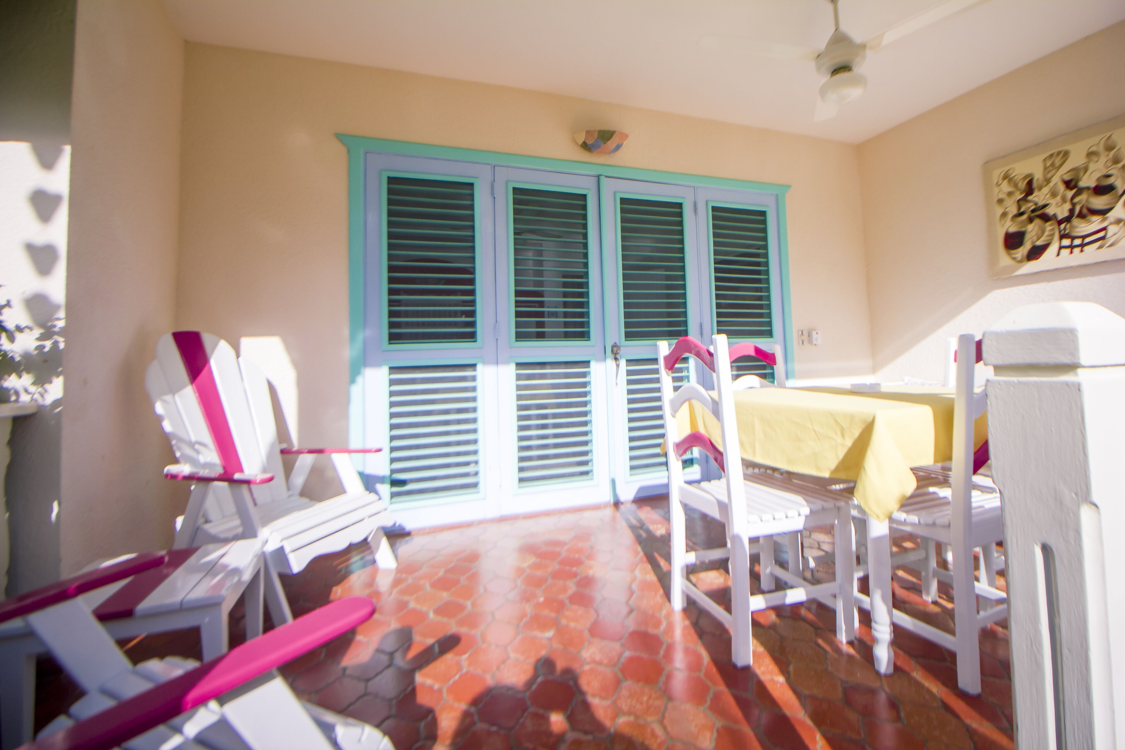 Une pièce avec un sol carrelé, une table recouverte d’une nappe jaune et un ventilateur au plafond.