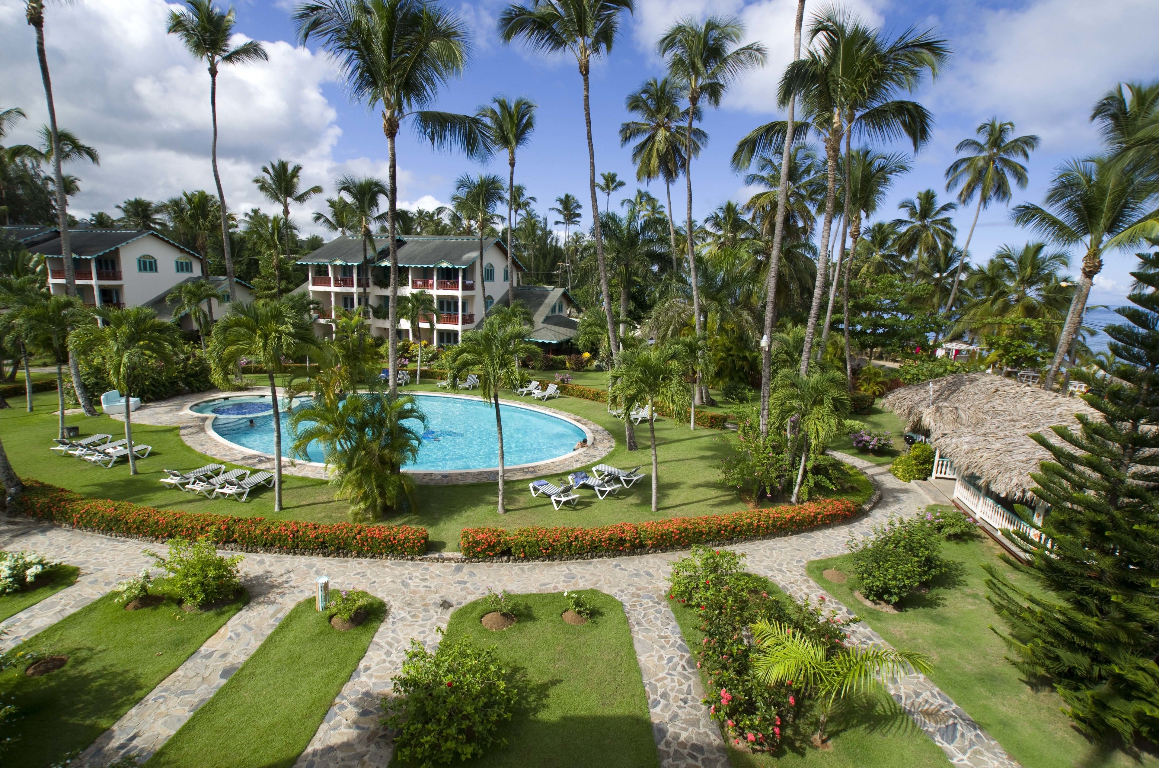 Un resort con piscina central, palmeras y césped cuidado.