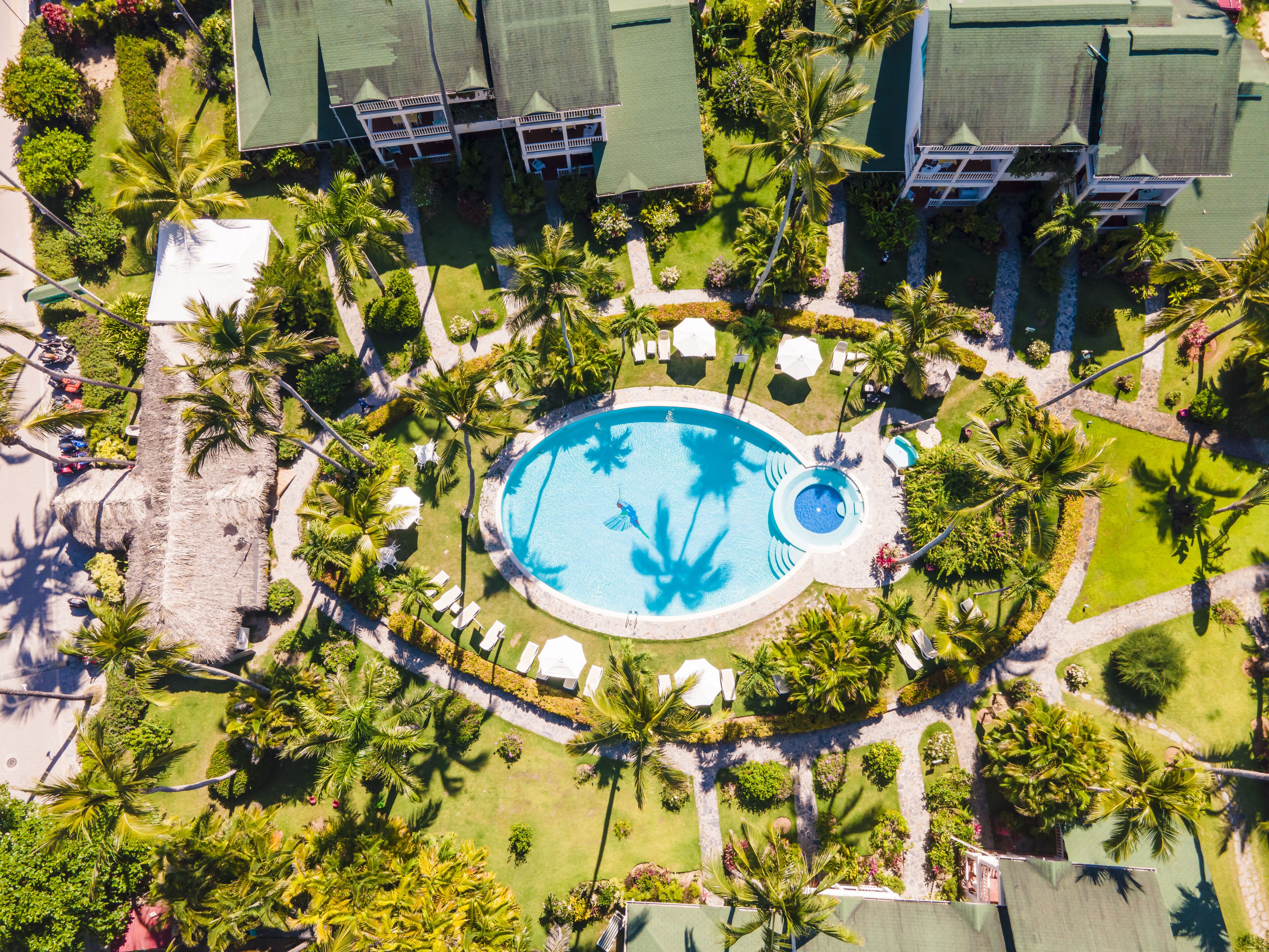 An aerial view of a resort with a central swimming pool, multiple lounge areas, and lush landscaping.