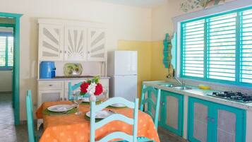 Une cuisine avec des meubles de couleur turquoise, un réfrigérateur blanc et une table à manger dressée avec des assiettes et un vase de fleurs.