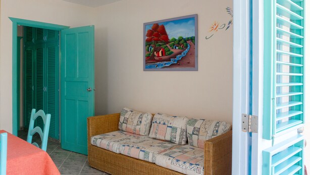 A room with a wicker sofa, a teal door, and a painting of a landscape. - Hotel Residence Playa Colibri (Las Terrenas)