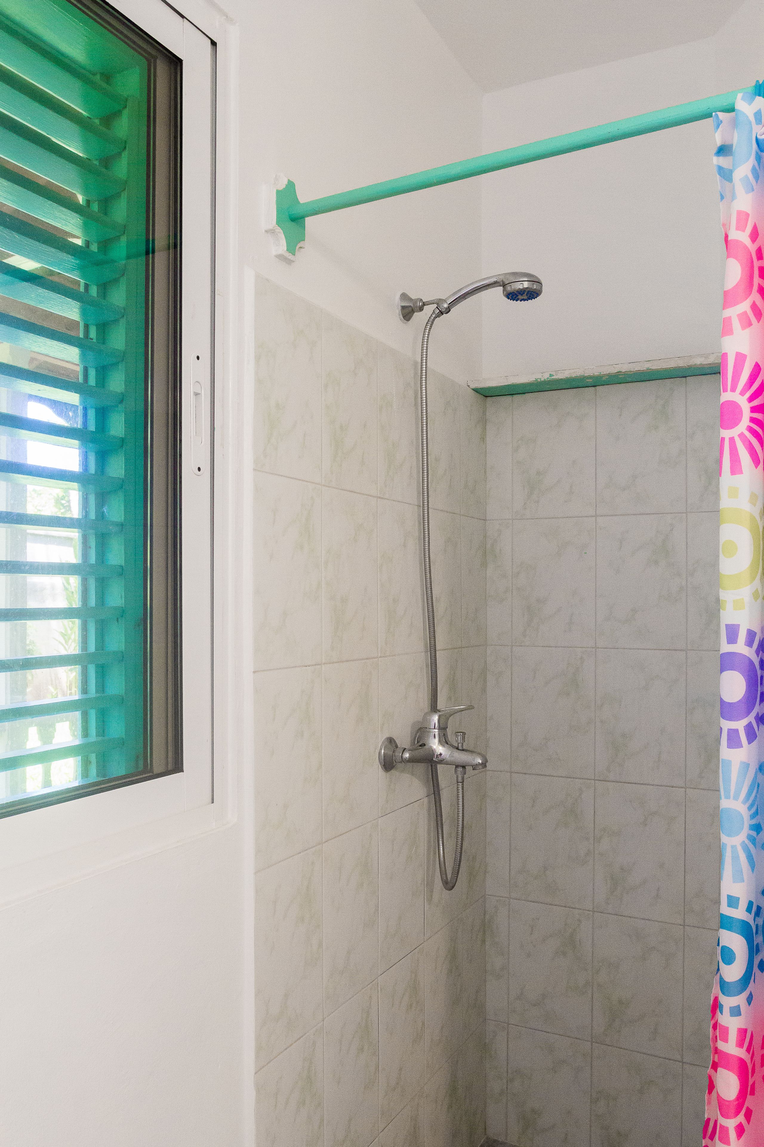 A shower with a handheld showerhead, a wall-mounted faucet, and a colorful shower curtain.